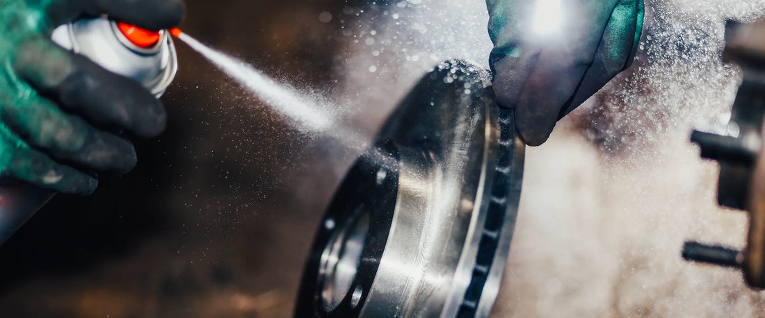 Person cleaning a metal wheel with a spray can of brake cleaner, wearing gloves.
